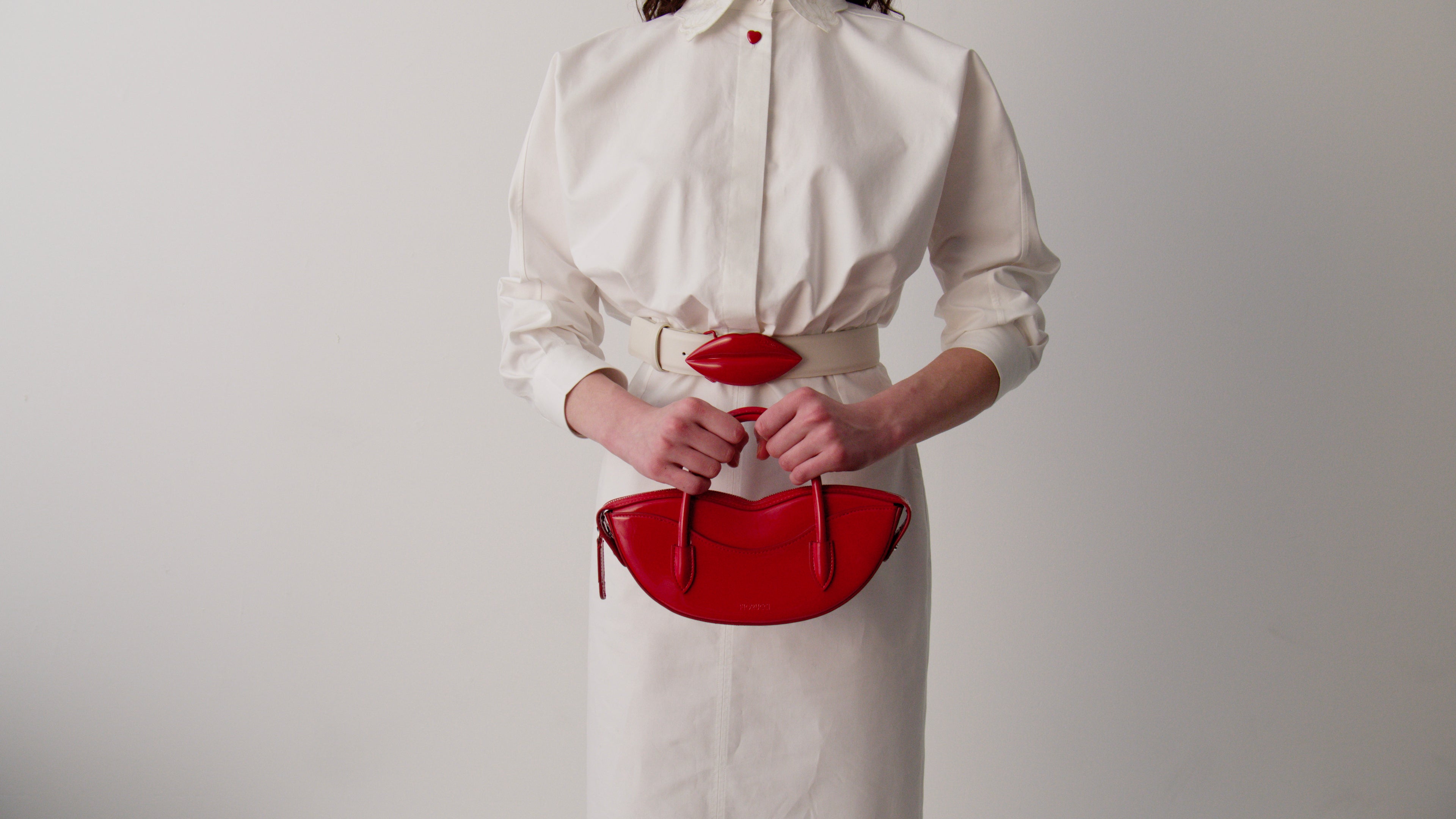 Model wearing a cream maxi dress with red lip print, belted at the waist, styled with red boots.